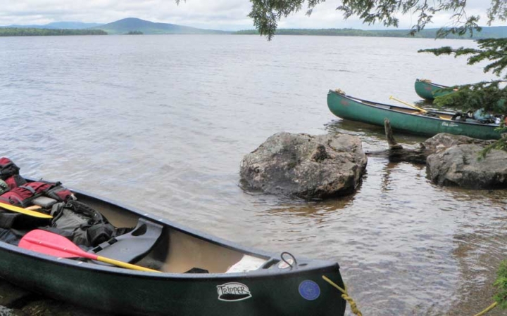Three empty canoes rest on the shore of a calm body of water.